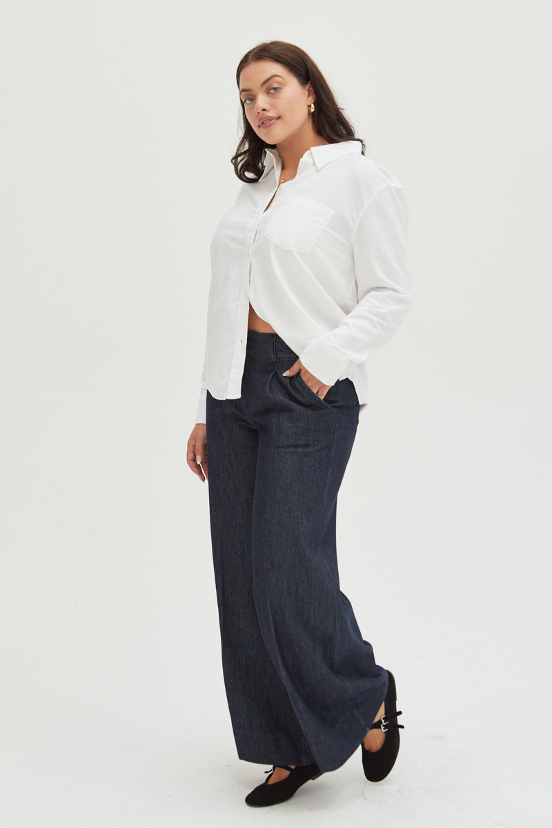 Side view of a curvy model in dark wash wide-leg trousers, styled with a sleek blazer, showcasing their timeless and versatile appeal.