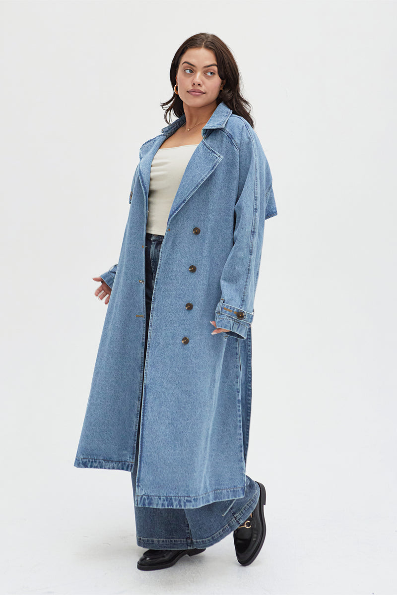 Side view of a curvy model in a light wash denim trench coat, showcasing its versatile and chic outerwear design.