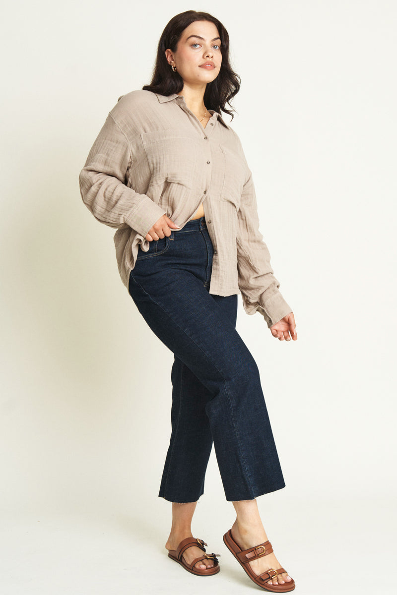 Side view of a plus-size model wearing a brown cotton button-up shirt and dark denim jeans.