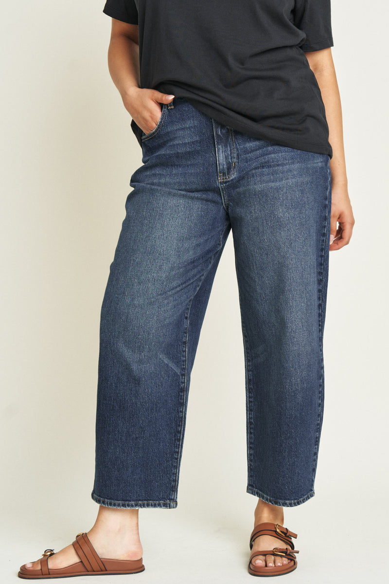 Close-up of high rise curved leg jeans, highlighting the dark blue denim texture and button closure.