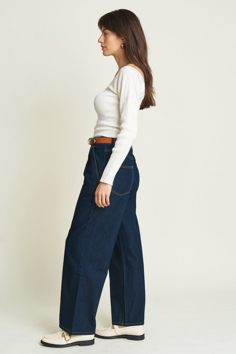 Side view of model in low-slung, dark blue baggy jeans, paired with white sneakers, showcasing their easygoing and versatile appeal.