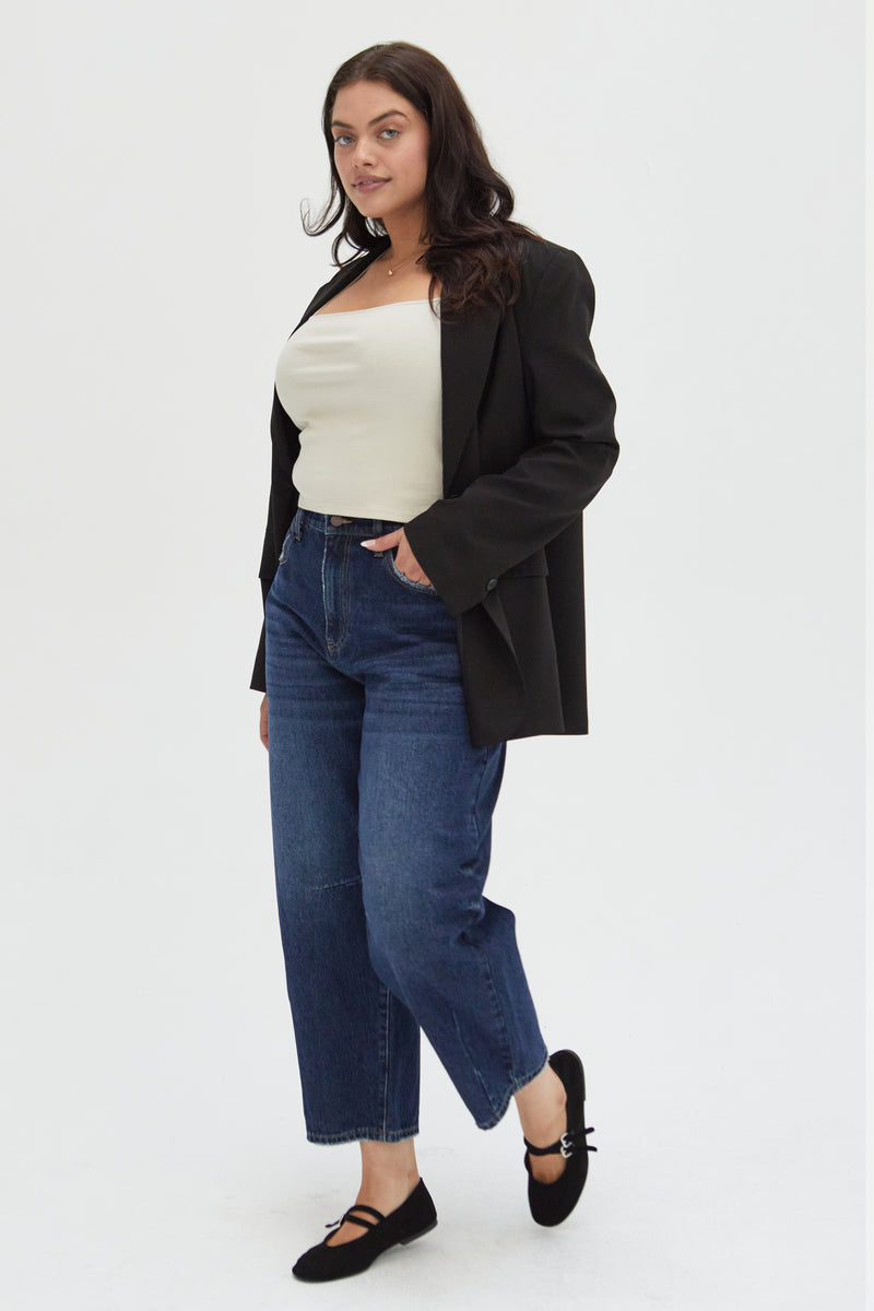 Side view of a plus-size model in barrel jeans, paired with a classic black blazer, showcasing a modern and versatile look.