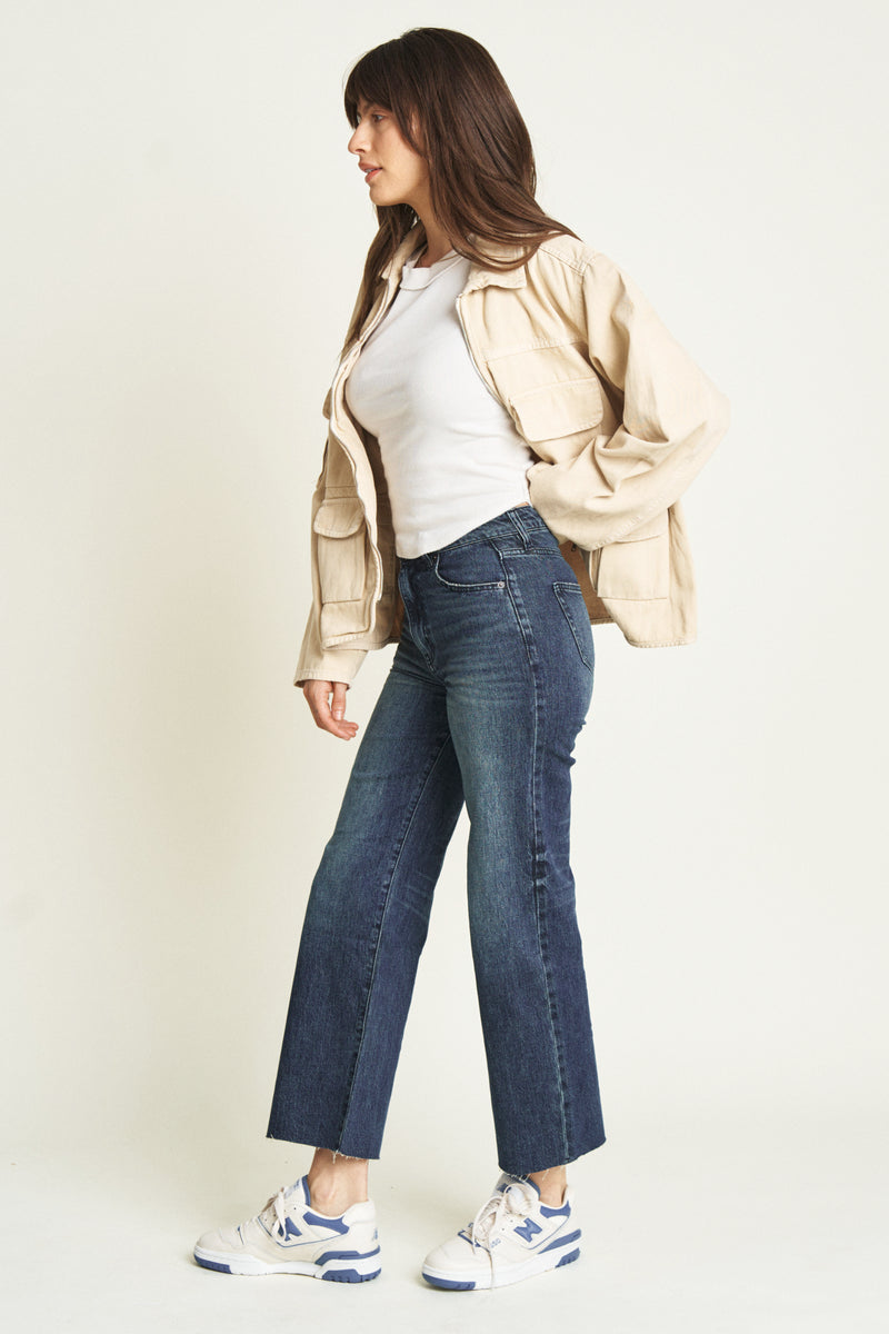 Side view of a model in dark blue ankle crop jeans, paired with a casual jacket, showcasing their modern and versatile style.