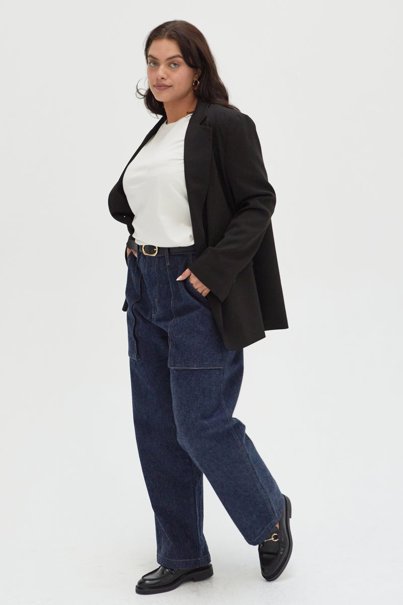 Side view of a plus-size model in trouser jeans, paired with a classic blazer, showcasing their versatile and elevated style.