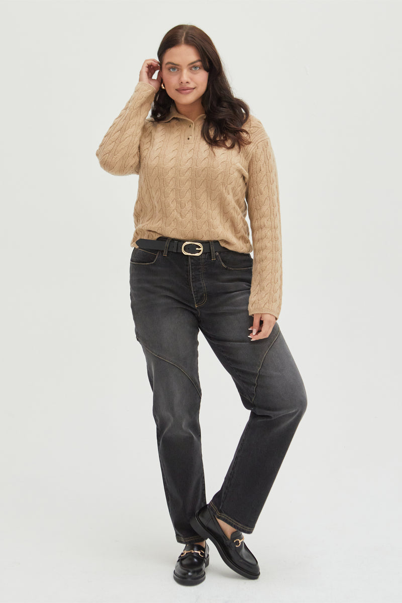  Plus-size model wearing high-rise straight leg jeans in a dark wash, styled with a tan cable-knit sweater and loafers, highlighting a relaxed fit and classic design.