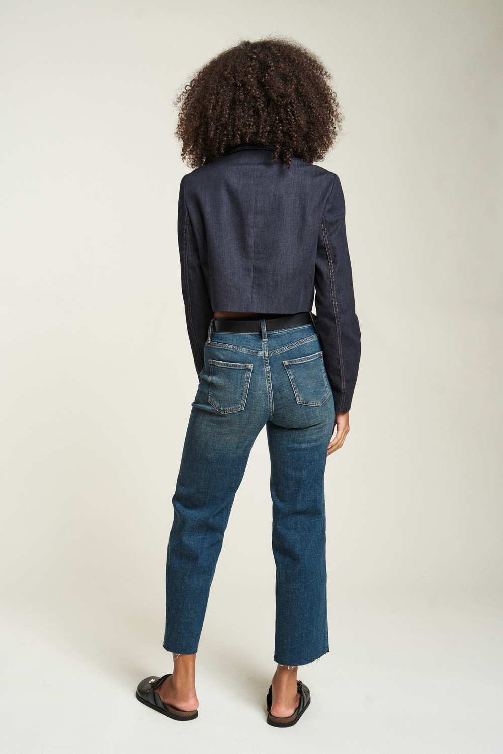 Back side of model wearing a black jacket showing the flattering fit of these high-rise jeans