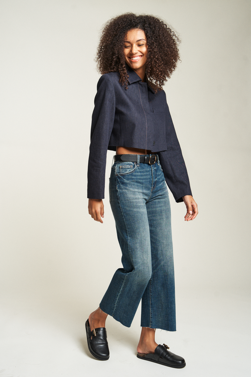 Side shot of model looking stylish in her black cropped jacket and dark blue cropped denim jeans.