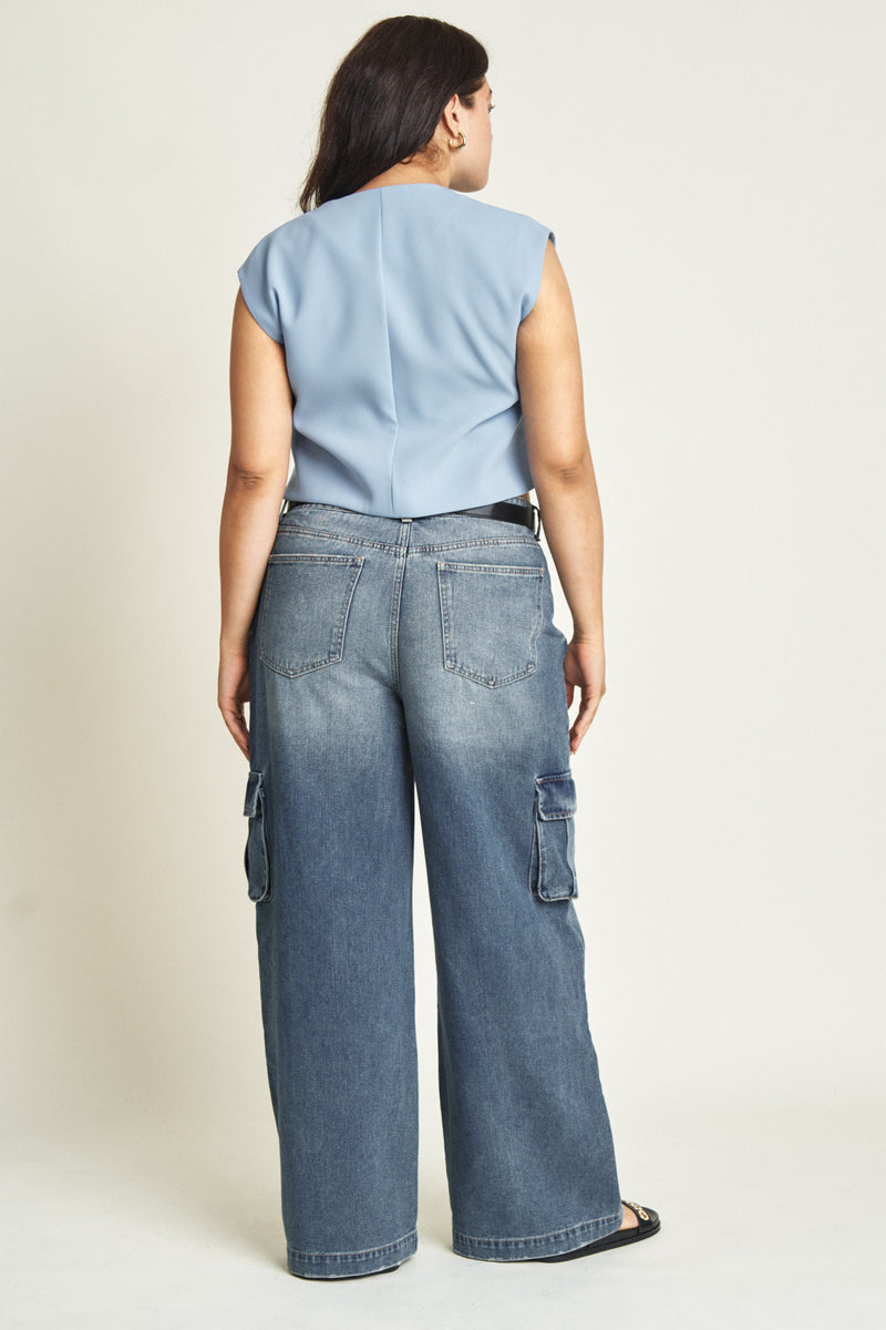 Back view of plus-size model in darker blue denim cargo jeans, showing high-rise fit and comfortable, sustainable design.