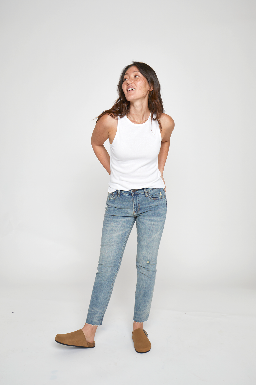 Petite model wearing high rise straight leg jeans in classic blue denim, paired with a white tank top, front view highlighting the slim fit.