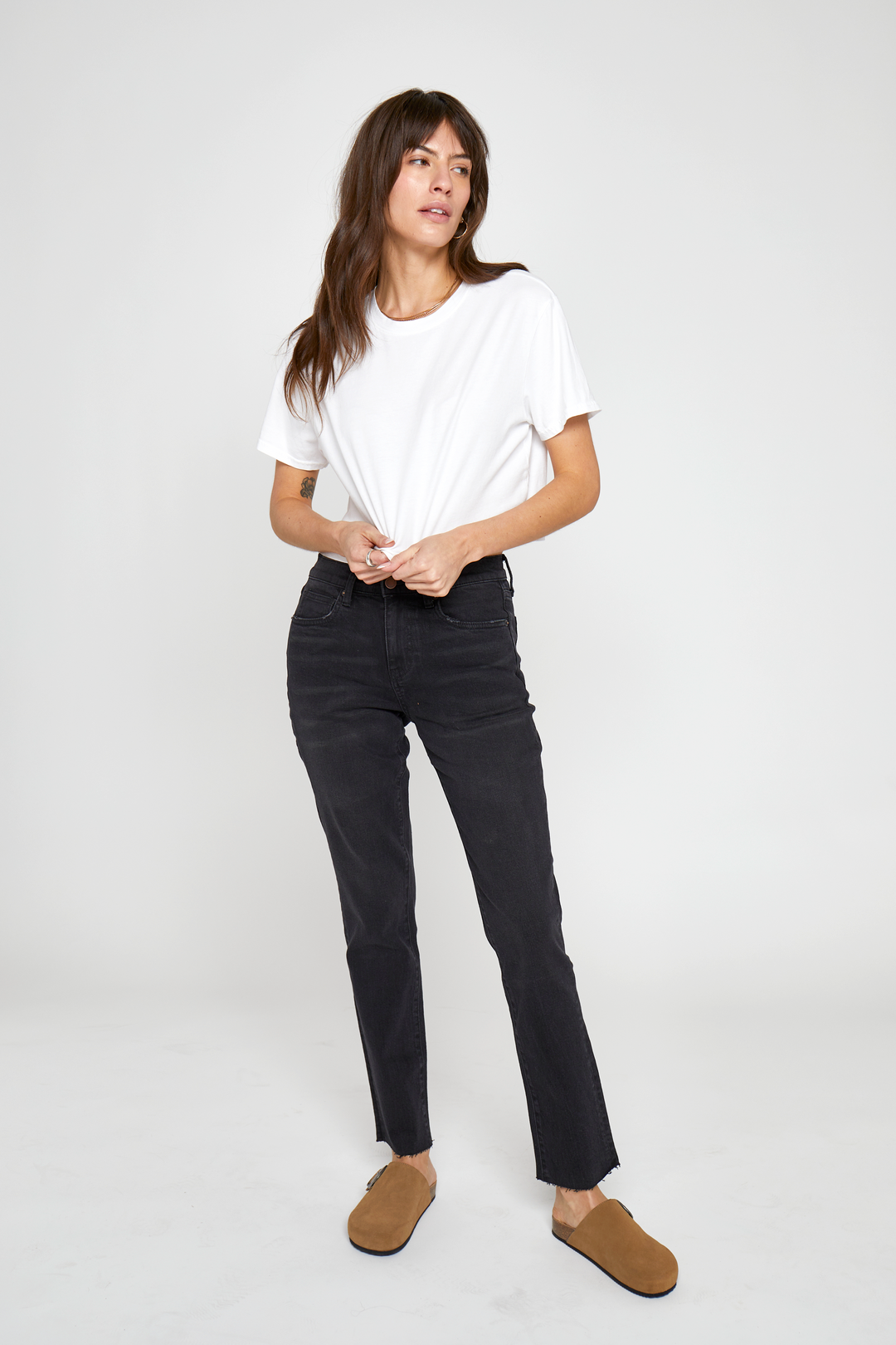 Model wearing high-rise tapered-leg jeans in a black wash, styled with a cropped white t-shirt and brown flats, showcasing a slim fit through the legs and flattering high-rise waist.
